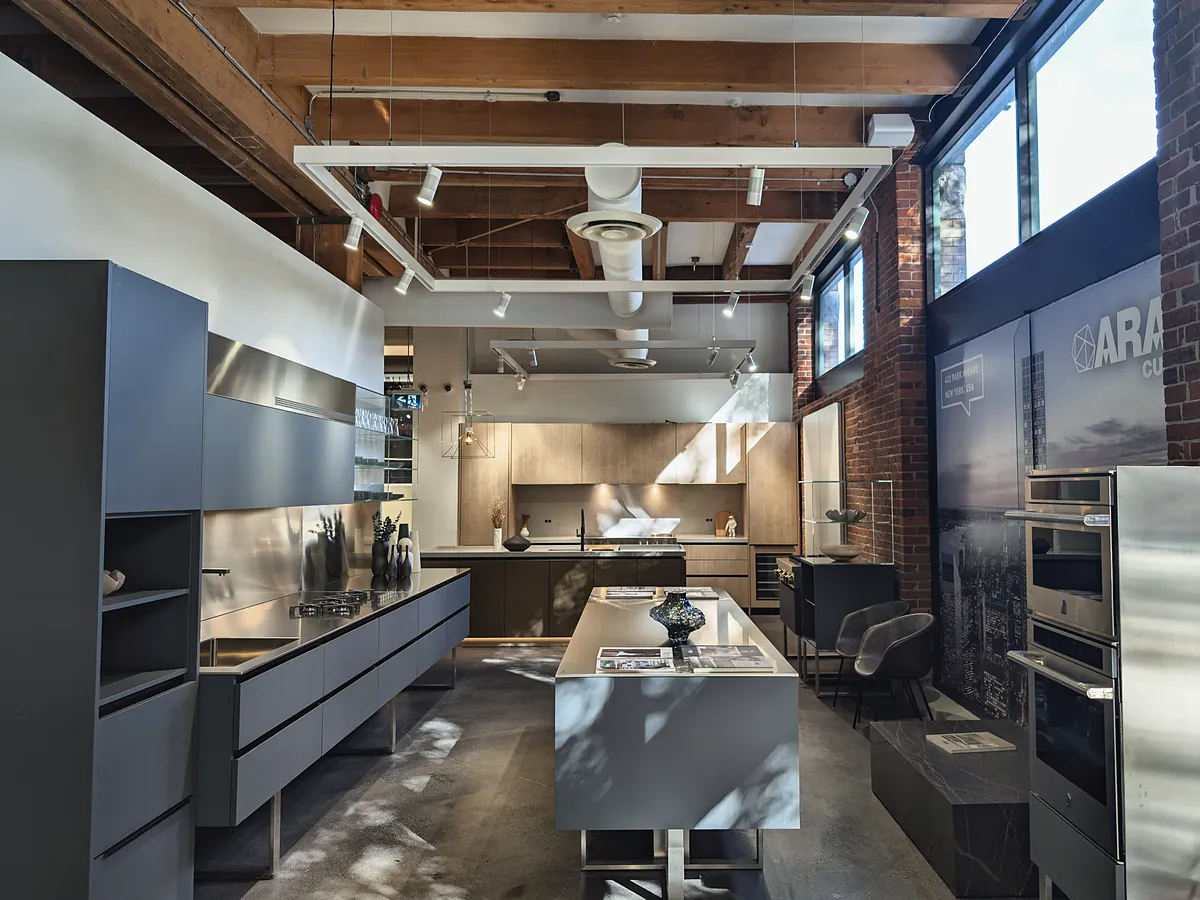 The showroom floor: staged kitchens, a brick wall with tall windows and exposed timber beams overhead.