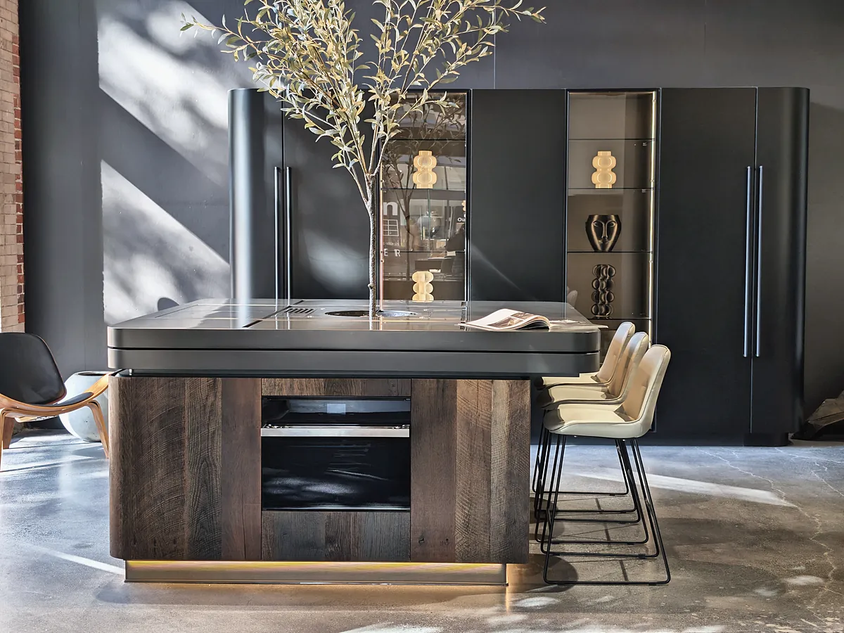 A dark oak kitchen island with a built-in oven, cream bar stools and a charcoal wall.